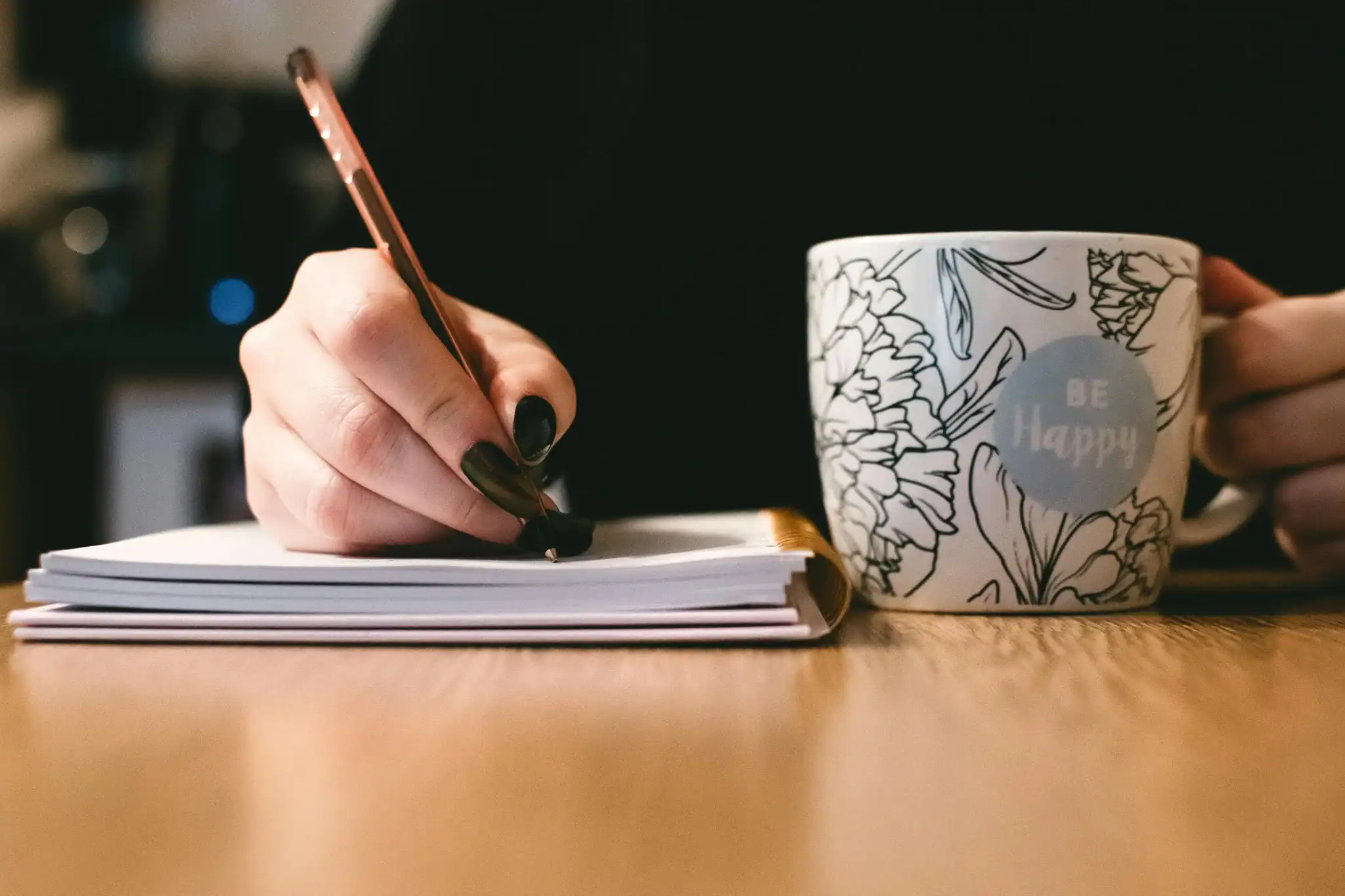 A person journaling with a 'Be Happy' mug in hand, symbolizing calm self-care during burnout recovery.