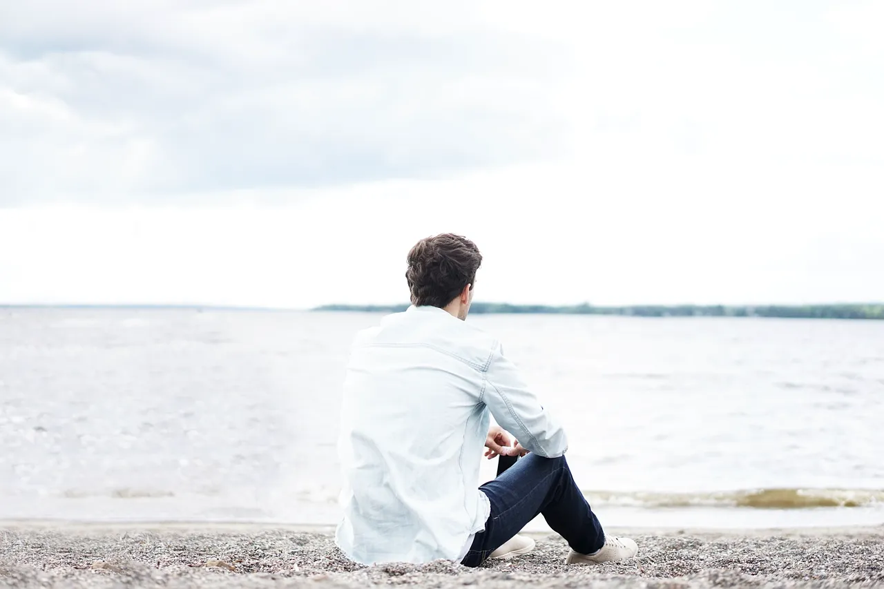 A man sitting alone on a beach, staring at the ocean, reflecting quietly – symbolizing emotional distance and disconnection from work.
