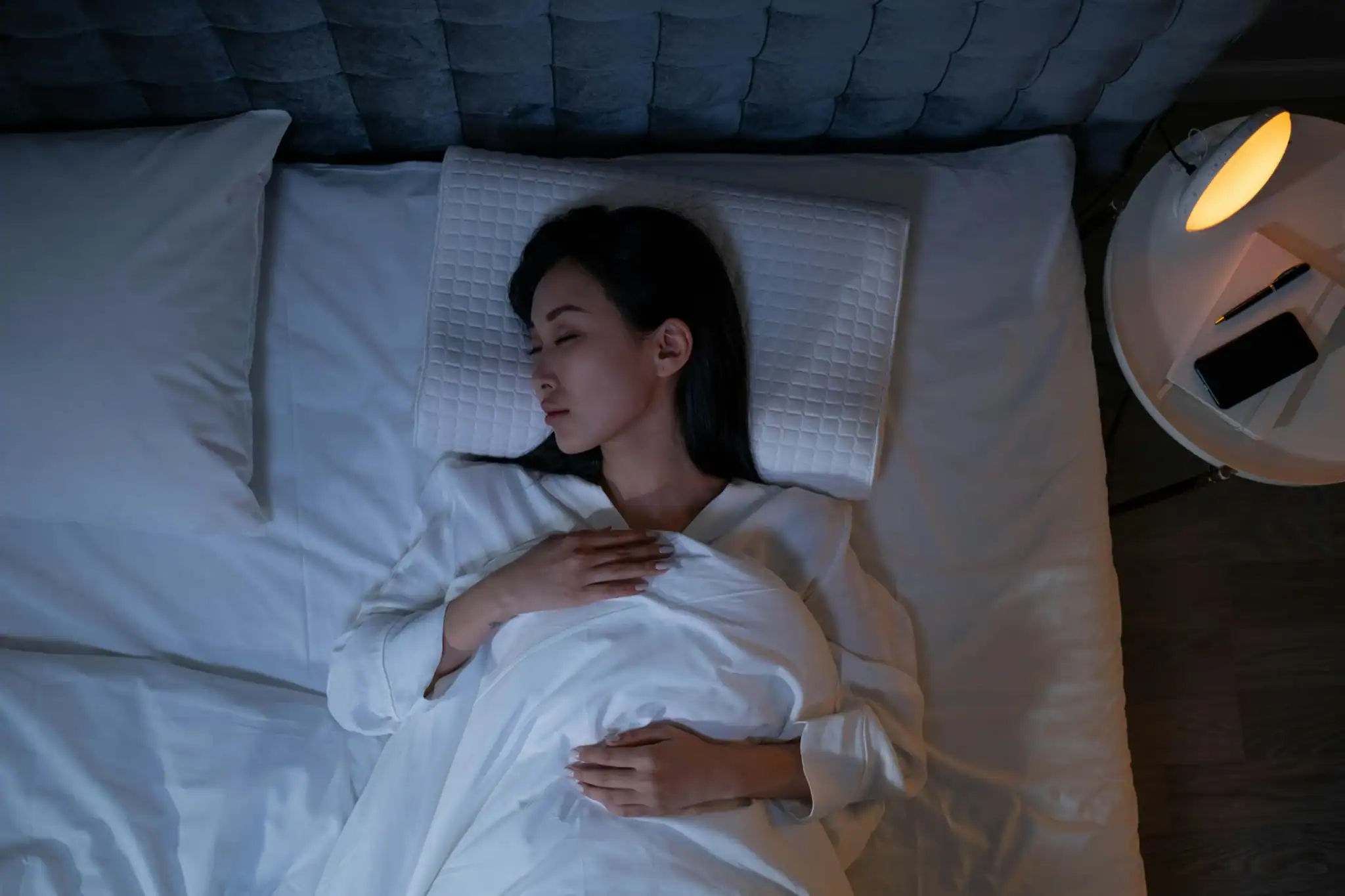 A peaceful woman sleeping in a cozy, dimly-lit bedroom, promoting healthy sleep routine