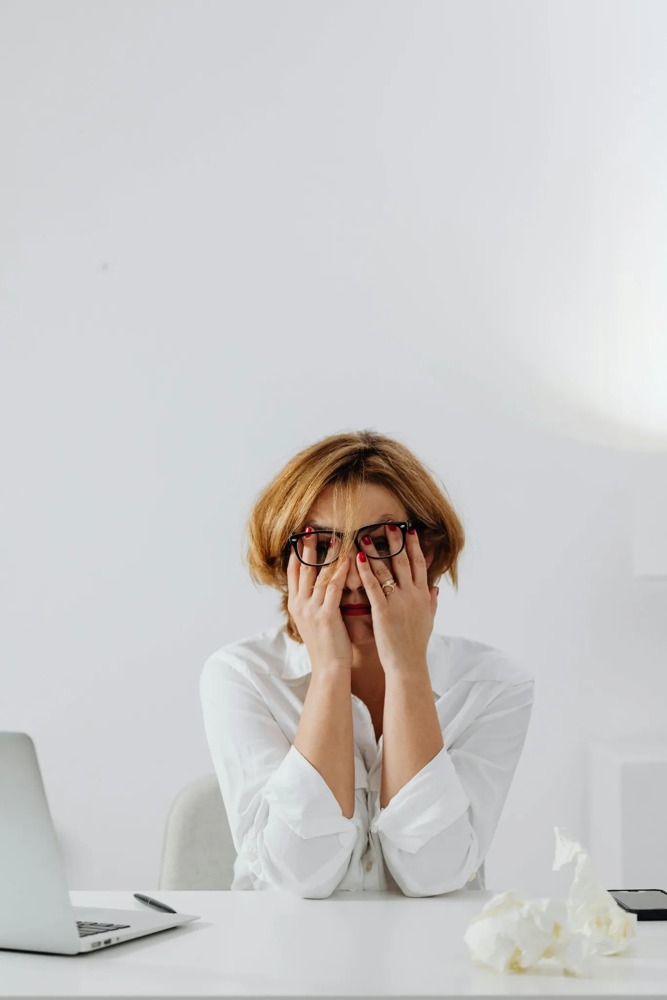 A stressed woman covering her face at work desk, overwhelmed by constant digital notifications.