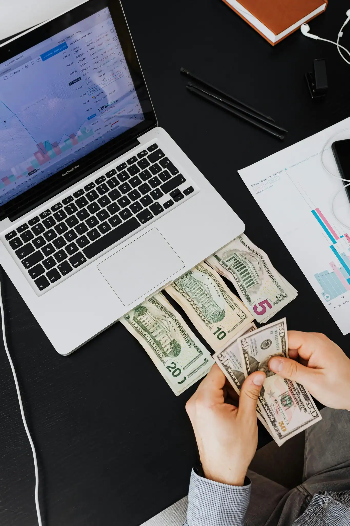 Remote worker managing cash and finances at desk with laptop and charts.