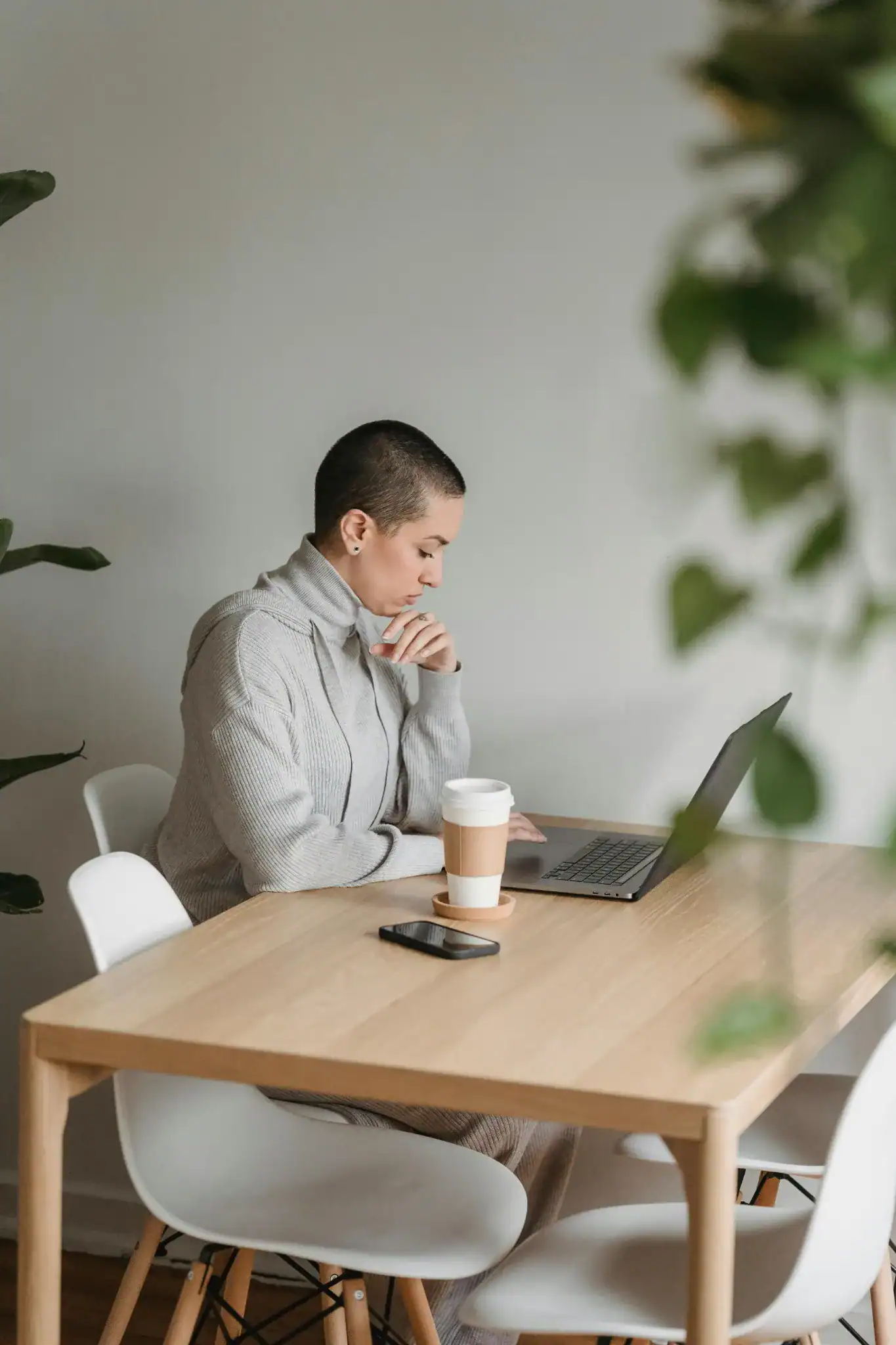 A focused remote worker sitting at a wooden table with a laptop and coffee cup, practicing mindful work in a calm home setting.