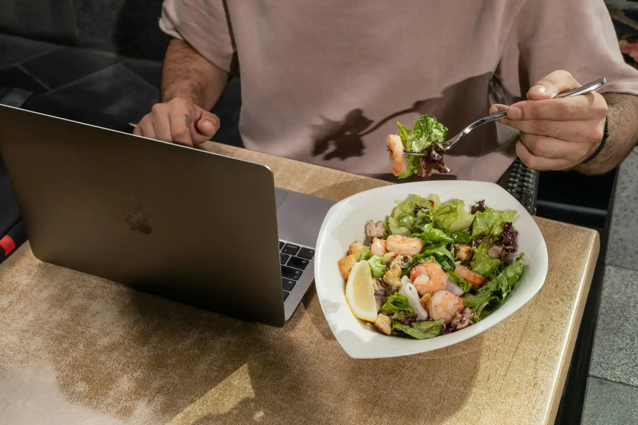 "Remote worker eating a healthy shrimp salad while working on a laptop"